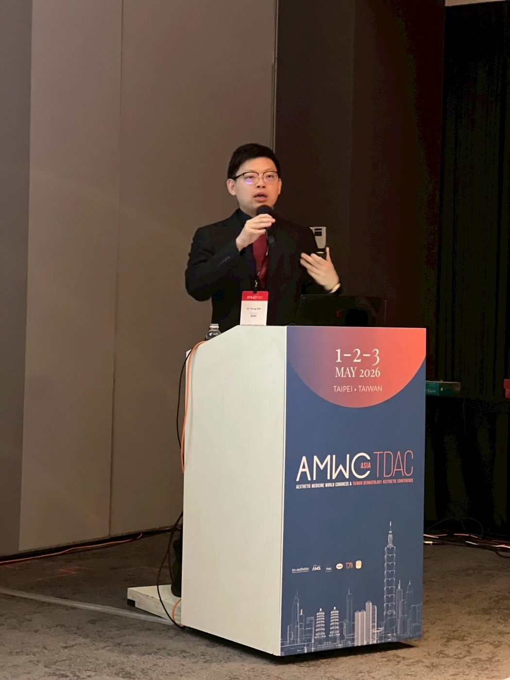 Dr. Sin Yong presenting at the AMWC Asia–TDAC 2026 lectern, Taipei, Taiwan